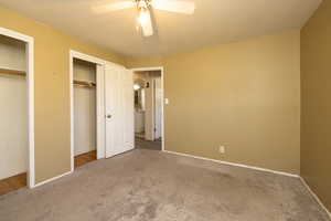 Unfurnished bedroom with carpet, two closets, and ceiling fan
