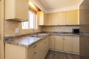 Kitchen featuring cream cabinets, dark wood-style flooring, stainless steel microwave, and backsplash