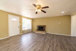 Unfurnished living room with a ceiling fan, dark wood-style flooring, a fireplace with raised hearth, a textured ceiling, and recessed lighting