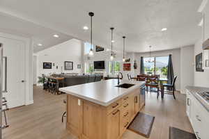 Kitchen featuring light brown cabinetry, light wood finished floors, recessed lighting, decorative light fixtures, and a kitchen island with sink