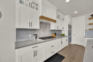 Kitchen featuring decorative backsplash, gas cook top, double ovens light wood-style floors, recessed lighting, open shelves, and white cabinets
