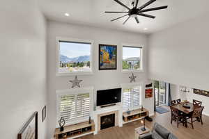 Views from the upper hallway of the Wasatch Mountains, main level living room featuring a ceiling fan, plenty of natural light, wood finished floors, a high ceiling, and a fireplace