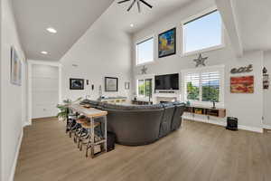 Living area featuring a high ceiling, light wood-style flooring, recessed lighting, a fireplace, and a ceiling fan, automatic-time able shades.