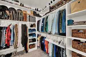 Primary suite spacious closet featuring carpet flooring, organizers, shelving and racks.
