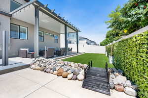 Awning and dry creek bed, featuring faux grass, potted plants with drip lines, solar lighting on the fence.