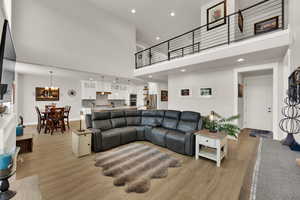 Living room featuring recessed lighting, light wood-style flooring, a towering ceiling, and a chandelier