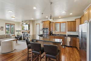 Kitchen with stainless steel appliances, open floor plan, wood finished floors, brown cabinetry, and recessed lighting
