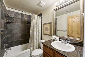 Bathroom featuring vanity, shower / tub combo, a textured ceiling, and a textured wall