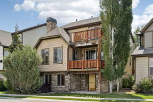 View of front of house featuring a balcony, a chimney, a shingled roof, stone siding, and a front yard