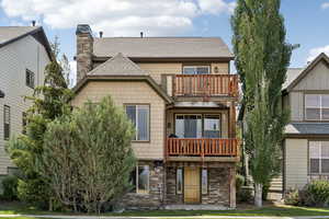 Rear view of house with a balcony, a chimney, a shingled roof, and stone siding