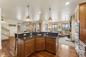 Kitchen with open floor plan, a kitchen bar, brown cabinetry, dark wood-style floors, and recessed lighting