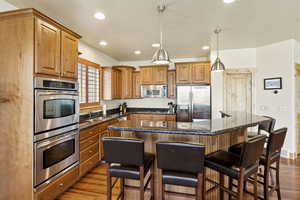 Kitchen with stainless steel appliances, wood finished floors, a kitchen breakfast bar, brown cabinetry, and recessed lighting