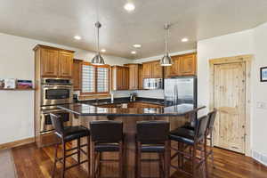 Kitchen featuring brown cabinets, stainless steel appliances, a kitchen breakfast bar, a kitchen island, and recessed lighting