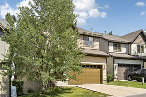 View of front facade with driveway, an attached garage, roof with shingles, and a front lawn