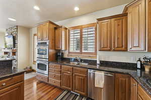Kitchen with stainless steel appliances, wood finished floors, recessed lighting, dark stone counters, and brown cabinetry
