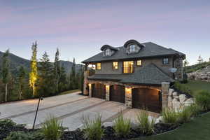 French country inspired facade featuring stone siding, driveway, stucco siding, a shingled roof, and an attached garage