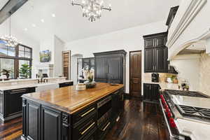 Kitchen with a chandelier, an island with sink, arched walkways, dark cabinetry, and high vaulted ceiling