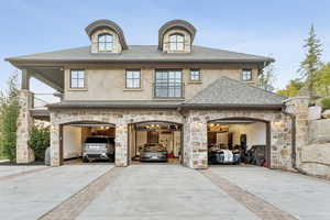 Back of house with concrete driveway, stone siding, stucco siding, and roof with shingles