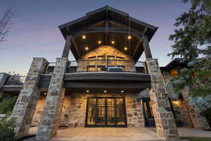 Back of house featuring a balcony, stone siding, and french doors
