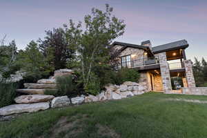 Rear view of house with stone siding, a balcony, a yard, and a chimney