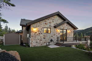 Rear view of property with a yard, a wooden deck, a storage unit, and stone siding