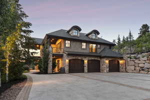 French country inspired facade featuring a balcony, driveway, an attached garage, stucco siding, and stone siding