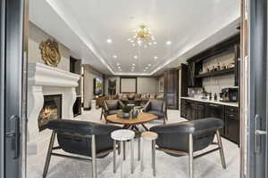 Living area with a raised ceiling, recessed lighting, a glass covered fireplace, wet bar, and light colored carpet