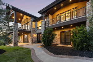 Rear view of house with a balcony, french doors, stone siding, a patio, and a lawn