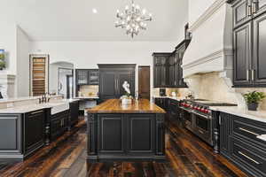 Kitchen with an island with sink, decorative backsplash, dark cabinetry, butcher block counters, and arched walkways
