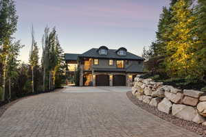 French provincial home featuring curved driveway, stone siding, a garage, and stucco siding