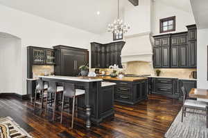 Kitchen with a kitchen island with sink, light countertops, decorative backsplash, high vaulted ceiling, and dark wood-style flooring