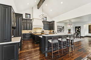 Kitchen featuring a center island with sink, beam ceiling, high vaulted ceiling, dark wood-style flooring, and a chandelier