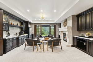 Living room with light colored carpet, bar with sink, a raised ceiling, recessed lighting, and a glass covered fireplace