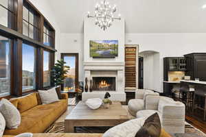 Living area featuring arched walkways, wood finished floors, a chandelier, a warm lit fireplace, and high vaulted ceiling