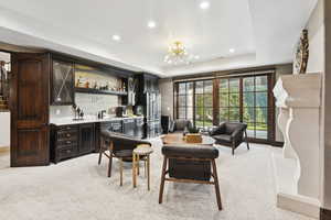 Living area with wet bar, a raised ceiling, light colored carpet, recessed lighting, and a chandelier