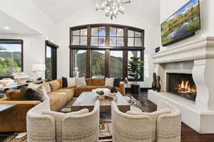 Living area featuring dark wood finished floors, a chandelier, a lit fireplace, a mountain view, and high vaulted ceiling