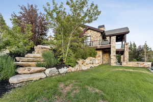 View of front facade with stone siding, a front yard, a balcony, and a chimney