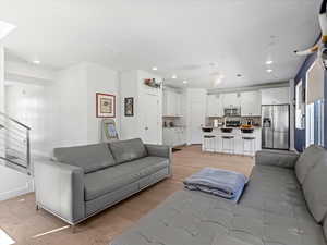 Living room with light wood-type flooring, recessed lighting, and stairway