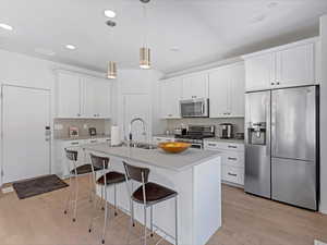 Kitchen featuring appliances with stainless steel finishes, tasteful backsplash, a breakfast bar area, a kitchen island with sink, and light countertops