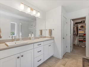 Full bathroom with double vanity, a shower stall, a walk in closet, and tile patterned floors