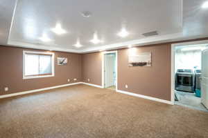 Empty room featuring washer and clothes dryer, a raised ceiling, and light colored carpet