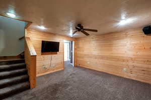 Unfurnished living room with wood walls, carpet flooring, a ceiling fan, stairs, and recessed lighting
