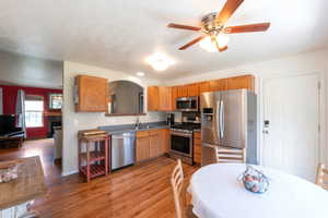 Kitchen with stainless steel appliances, light wood finished floors, a ceiling fan, and a textured ceiling