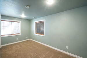 Carpeted empty room with a textured ceiling and a smoke detector