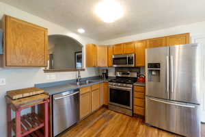 Kitchen featuring appliances with stainless steel finishes, light wood finished floors, dark countertops, a textured ceiling, and arched walkways