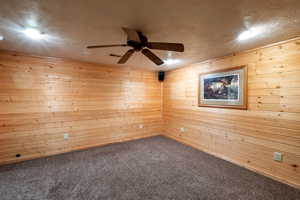 Empty room with carpet flooring, wood walls, and ceiling fan