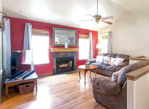 Living room with a tiled fireplace, ceiling fan, wood finished floors, and lofted ceiling