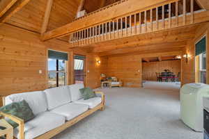 Carpeted living room featuring high vaulted ceiling, a wood ceiling with exposed beams, and wood walls