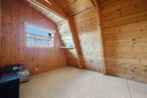 Empty room with vaulted ceiling, wood walls, carpet flooring, and wood ceiling