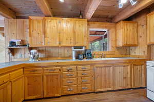 Kitchen with tile counters, light brown cabinets, light wood-style flooring, a wood ceiling with exposed beams, and wood walls